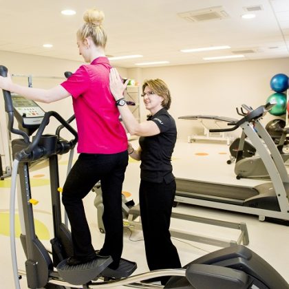 An exercise physiologist guides a patient through an exercise on an elliptical trainer