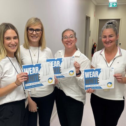 Staff smiling holding up a sign 'Wear white for mental health'.