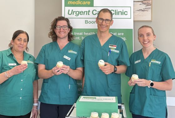 Booragoon UCC team smile whilst holding branded cupcakes in front of a branded pull up banner