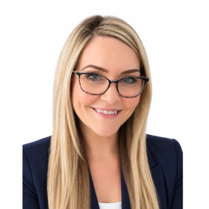 Alex smiles at the camera, she has light hair. she is wearing black glasses and a black jacket.